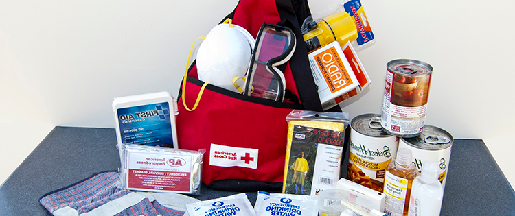 一个红色背包，里面装着包装好的食物和水、安全眼镜、防尘口罩和急救用品.